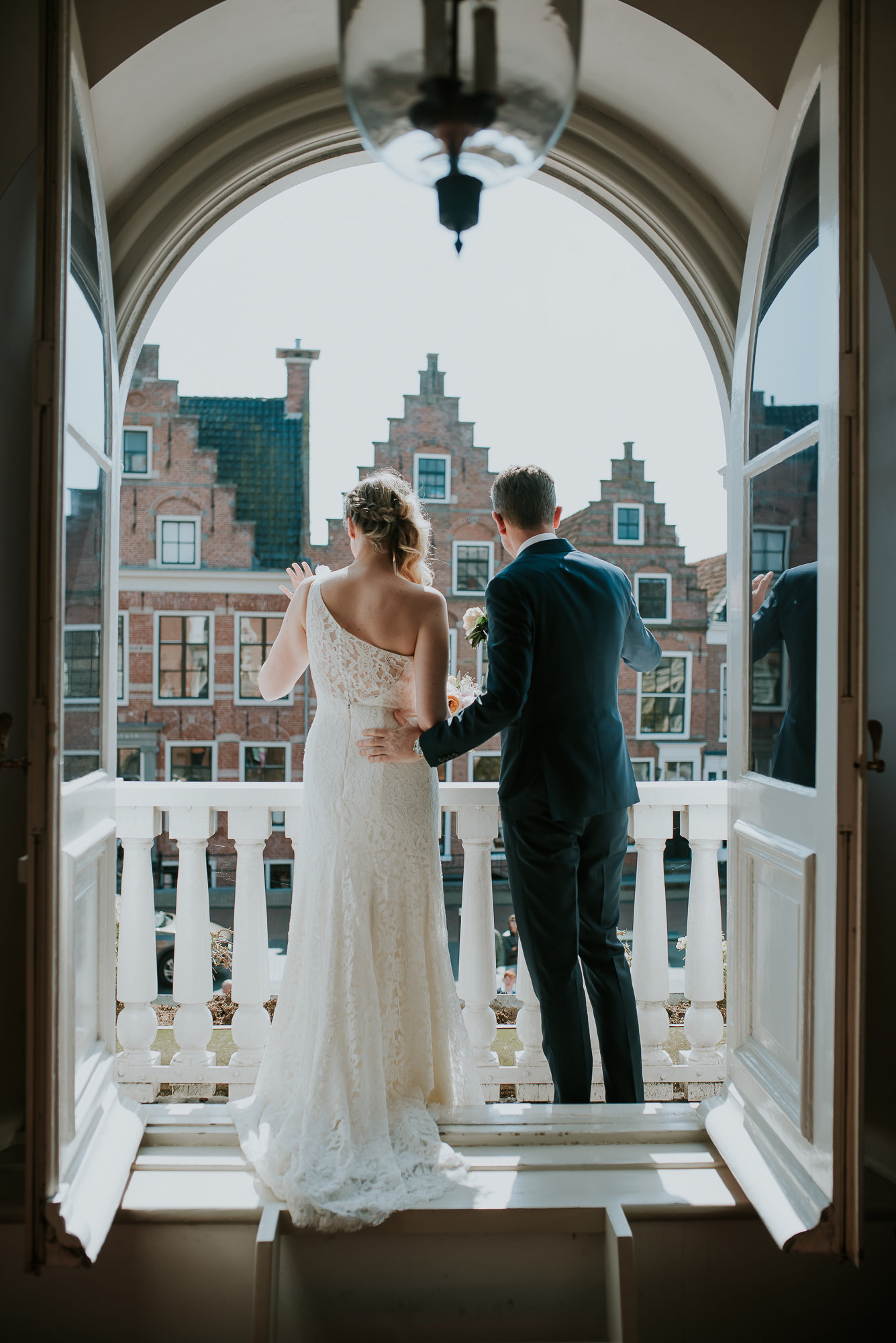 Het bruidspaar zwaait vanaf het balkon naar de gasten. Huwelijksfotografie door huwelijksfotograaf uit Dokkum, Friesland.