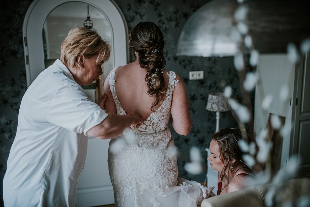 Moeder en tweelingzus helpen met het aankleden van de bruid. Trouwreportage door trouwfotograaf NIckie Fotografie uit Dokkum, Friesland.