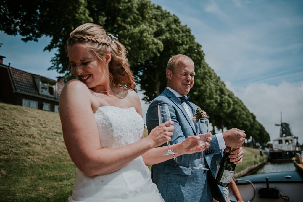 Bruidegom ontkurkt de champagnefles op de boot in Dokkum. Trouwreportage door trouwfotograaf Nickie Fotografie uit Friesland