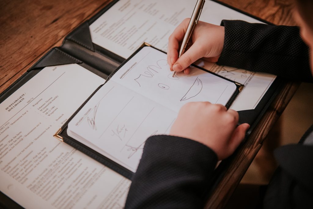 Zoon ondertekent de huwelijksakte door een mooie tekening in het trouwboekje te maken. Huwelijksfotografie door huwelijksfotograaf Nickie Fotografie uit Dokkum, Friesland