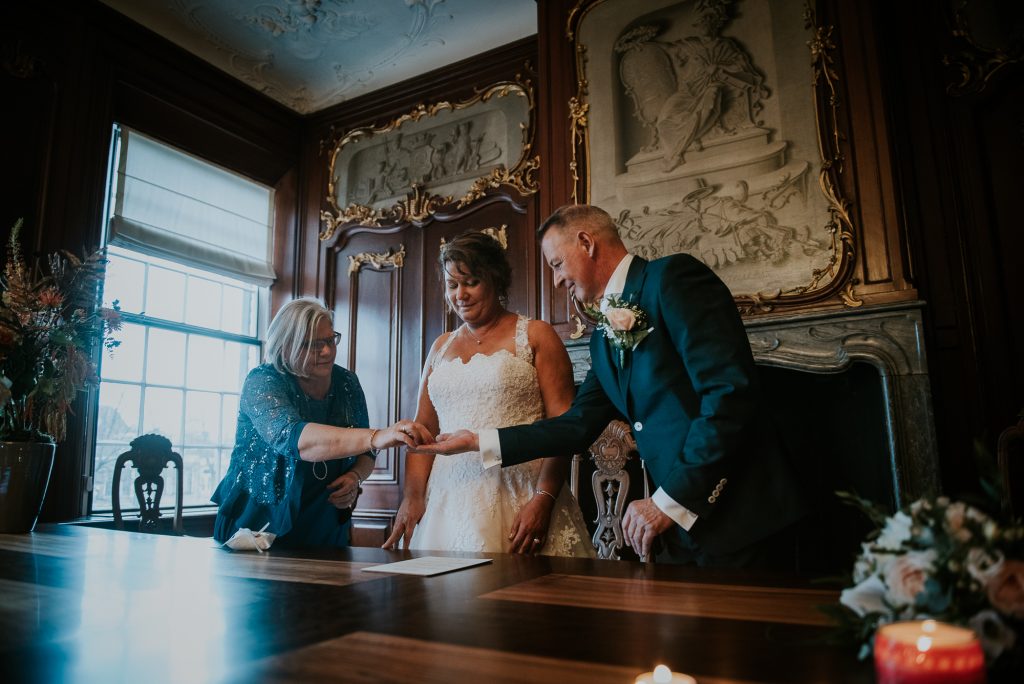 Het ringenmeisje/ringdrager overhandigt de trouwringen aan het bruidspaar in de trouwzaal. Huwelijksfotografie door huwelijksfotograaf Nickie Fotografie.