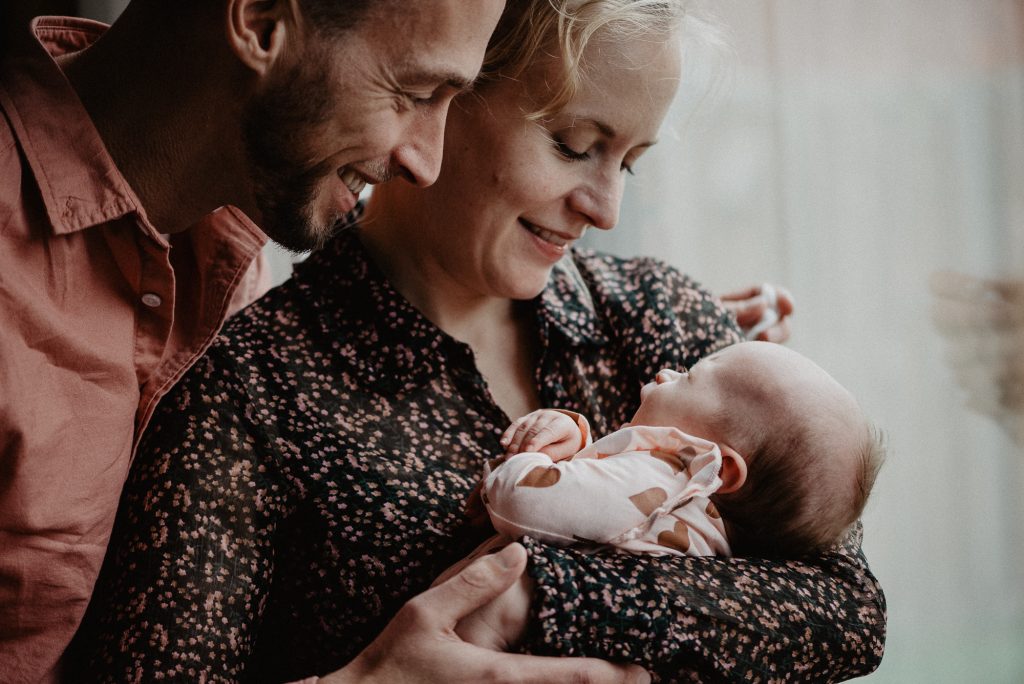 Newborn fotoshoot Friesland, Drachten, door fotograaf Nickie Fotografie. Vader en moeder bewonderen hun pasgeboren dochter.