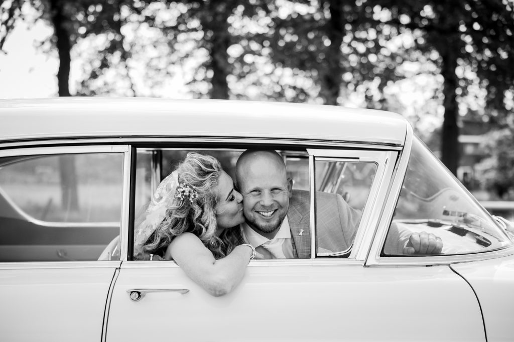 Bruid kust haar bruidegom in de prachtige Cadillac bruidsauto. Trouwreportage door trouwfotograaf NIckie Fotografie.
