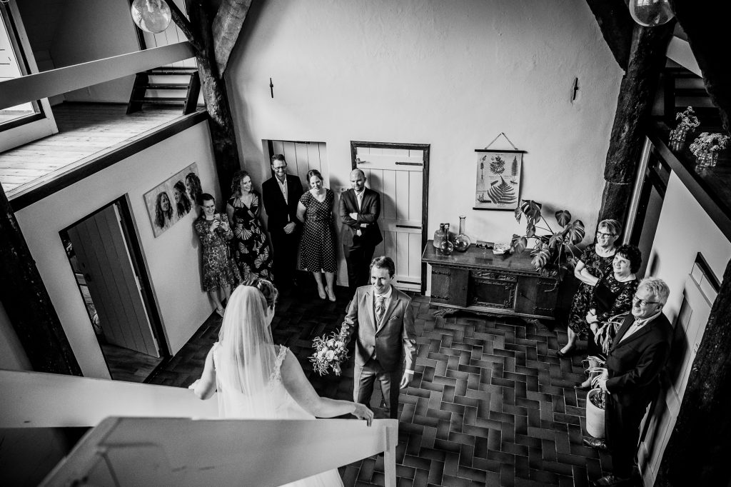 First look tussen bruid en bruidegom wanneer de bruid van de trap af komt in oude boerderij. Bruidsfotografie door bruidsfotograaf Nickie Fotografie uit Dokkum, Friesland.