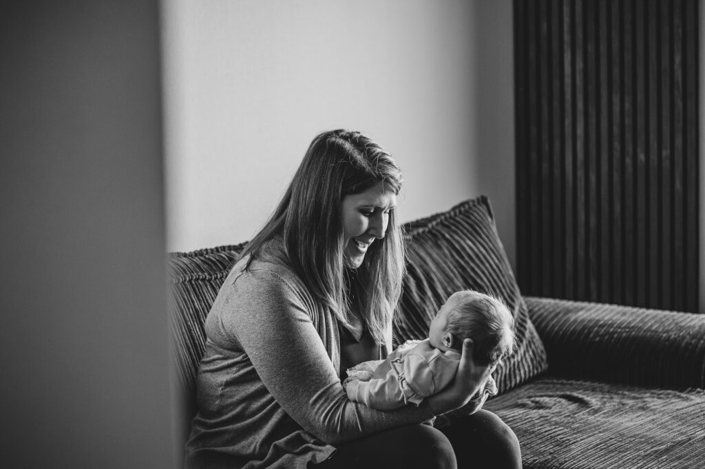 Zwartwit newbornreportage door fotograaf Nickie Fotografie uit Dokkum, Friesland. Moeder kijkt haar baby aan terwijl ze haar op schoot heeft.