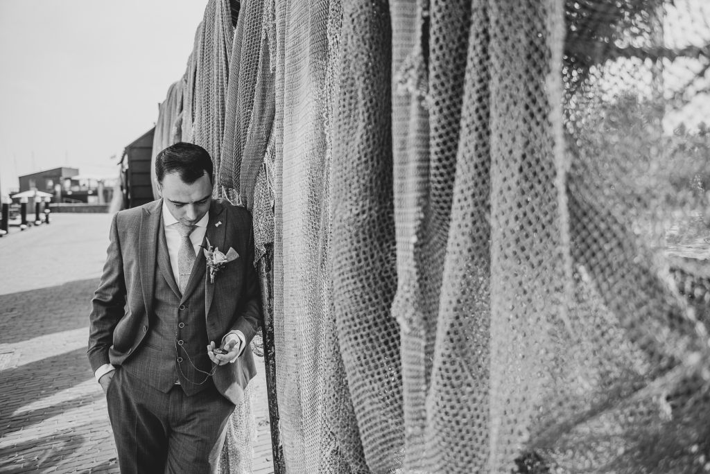 Bruidegom kijkend op zijn zakhorloge bij de vissersnetten in de botterhaven van Urk, Trouwreportage door trouwfotograaf Nickie Fotografie .