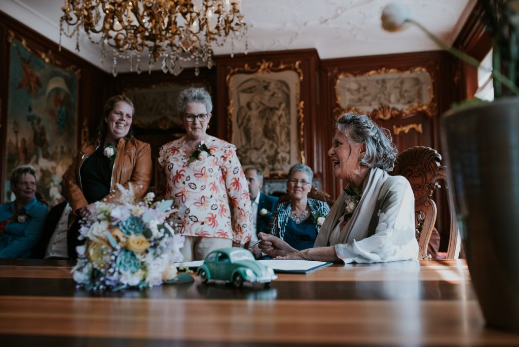 Moeder van de bruidegom ondertekent de trouwakte in de trouwzaal van Dokkum. Trouwfotografie door fotograaf NIckie Fotografie.
