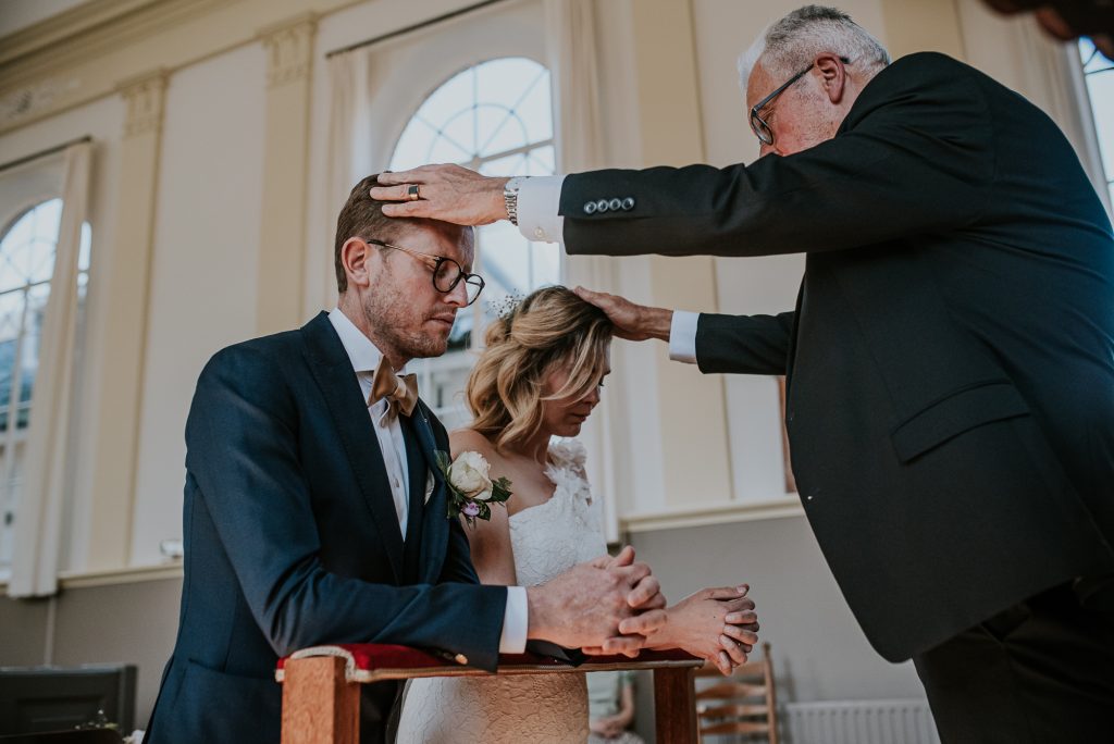 Bruid en bruidegom ontvangen hun zegening van de voorganger/dominee in Dokkum. Bruidsfotografie door bruidsfotograaf Nickie Fotografie uit Friesland.