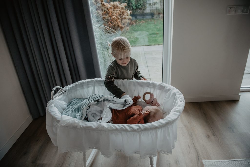 Grote zus stopt babyzusje in. Lifestyle newbornshoot Friesland, Leeuwarden, door fotograaf Nickie Fotografie.