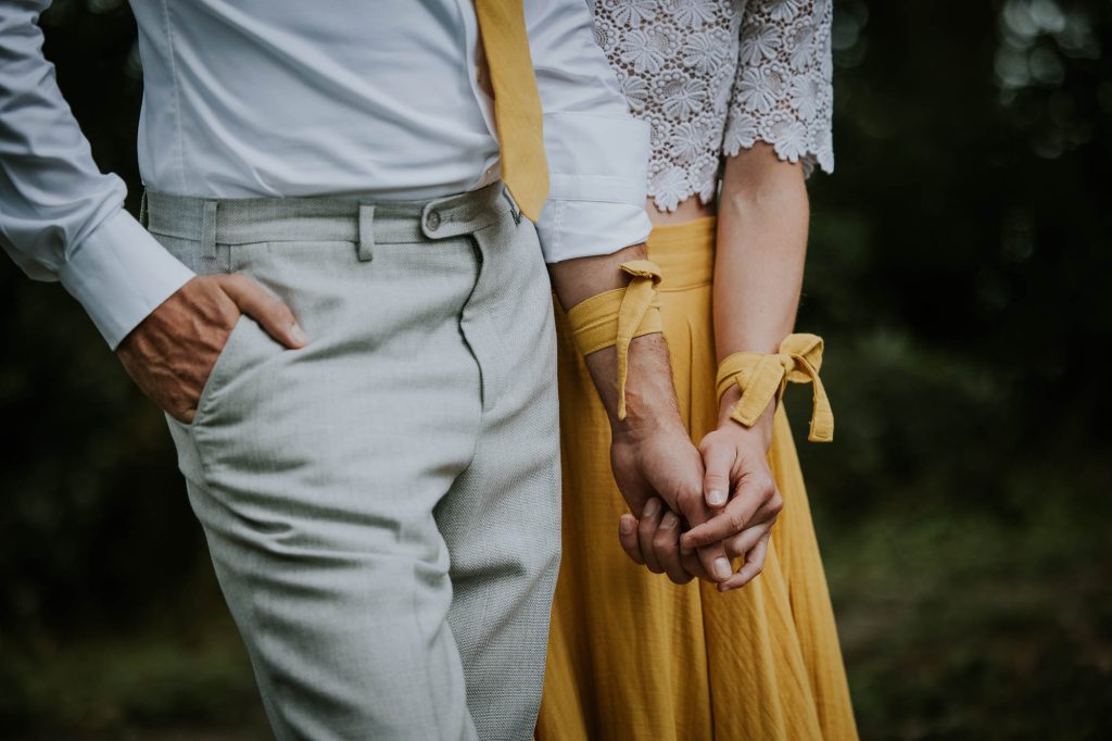 Het bruidspaar draagt gele linten om de pols om hun huwelijks tattoo te verbergen. Trouwshoot door huwelijksfotograaf Nickie Fotografie.