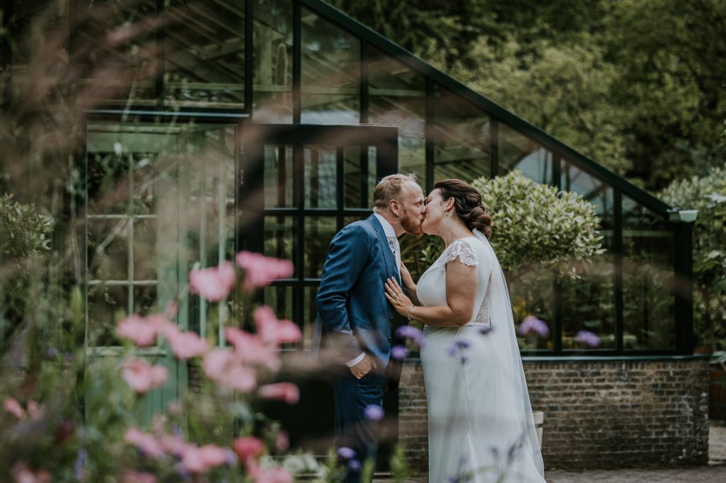 Het bruidspaar kust elkaar na de first look bij de tropische kas in Beetsterzwaag. Huwelijksreportage door huwelijksfotograaf Nickie Fotografie uit Friesland.