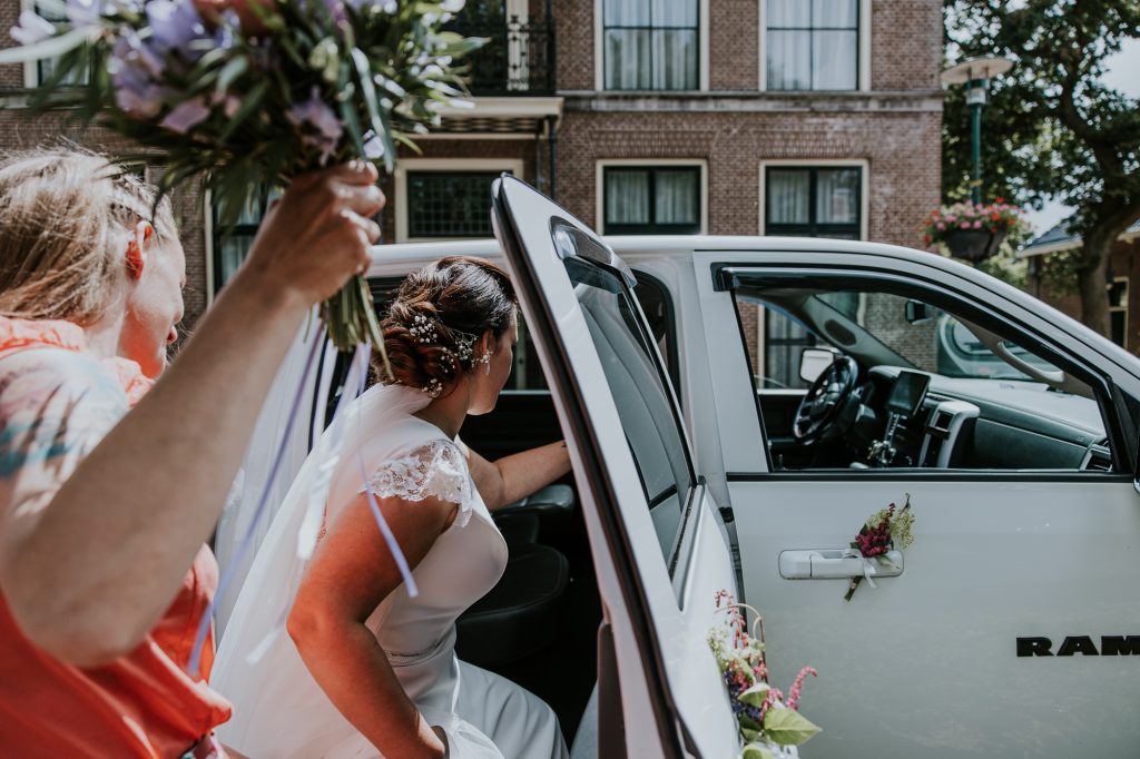 Bruid stapt in de witte Chevy die dienst doet als gave trouwauto. Trouwshoot door trouwfotograaf Nickie Fotografie uit Friesland.