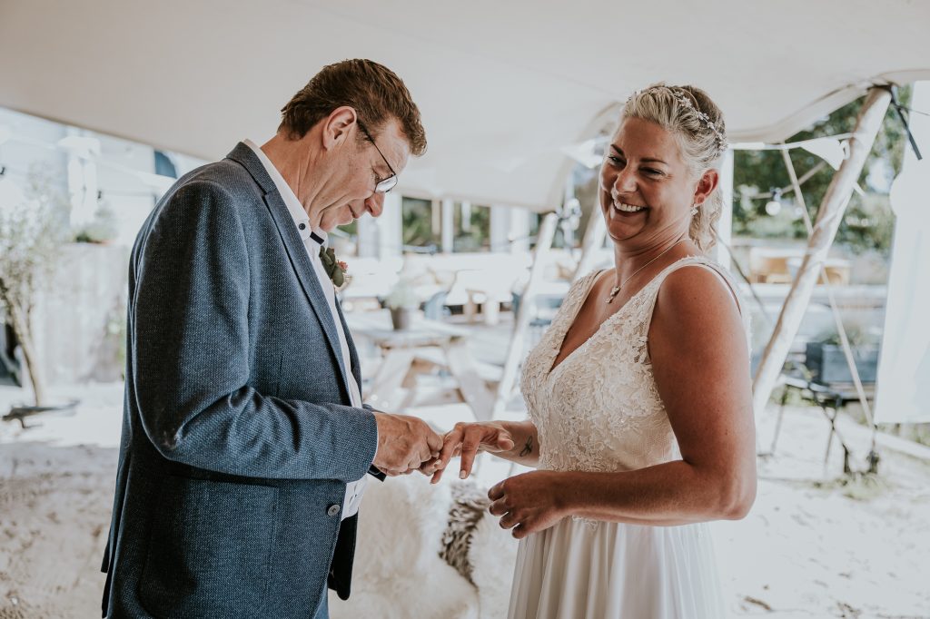 Het uitwisselen van de trouwringen tijdens de huwelijksceremonie in een tent bij paviljoen Schreiershoek vlakbij Dokkum door huwelijksfotograaf NIckie Fotografie.