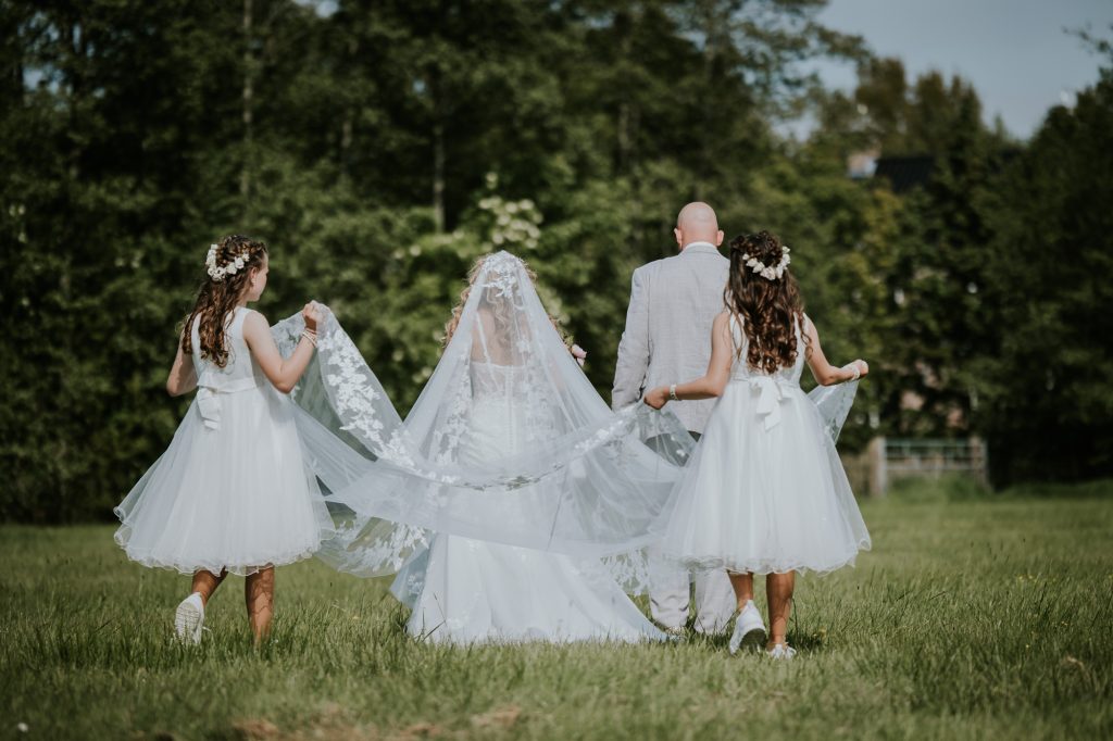 Trouwen in Friesland. Bruidsmeisjes houden de prachtige lange sluier van de bruid beet. Huwelijksfotografie door huwelijksfotograaf Nickie Fotografie.