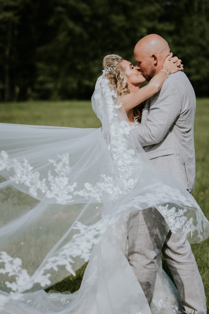 Kussend bruidspaar met wapperende prachtige sluier. Bruidsshoot door trouwfotograaf Nickie Fotografie uit Dokkum.