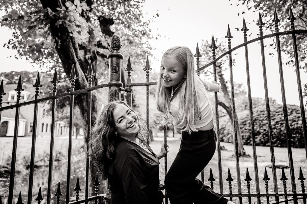 Speelse moeder en dochter fotoshoot bij groot metalen hek door fotograaf Nickie Fotografie.