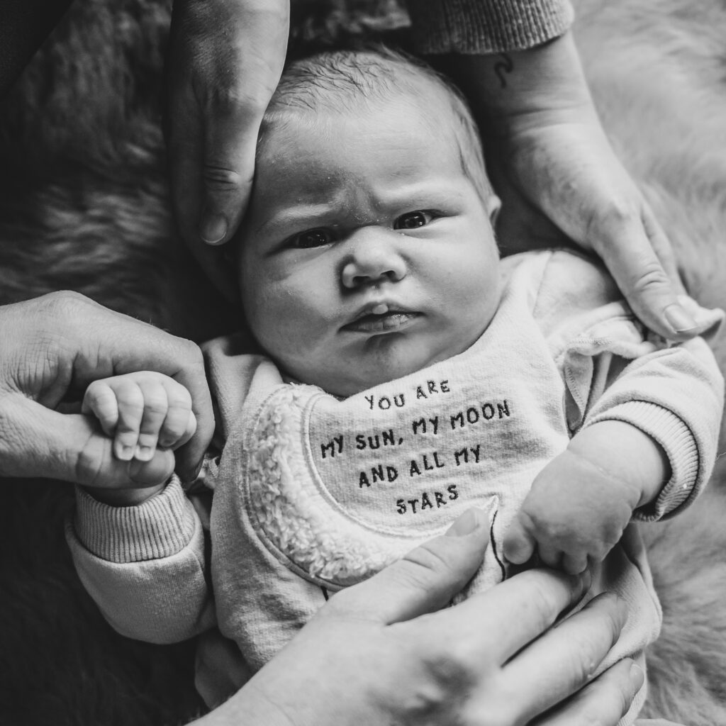 Zwartwit babyreportage. Baby kijkt met zeer ernstige blik naar de camera.  Babyfotografie door fotograaf Nickie Fotografie uit Dokkum, Friesland.