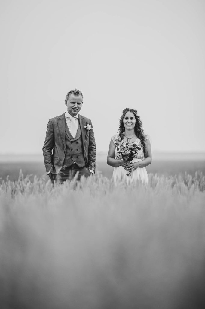 Fotoreportage tijdens de bruiloft. Het bruidspaar staat in een graanveld. Zwart-wit bruidsreportage door trouwfotograaf Nickie Fotografie uit Dokkum, Friesland.