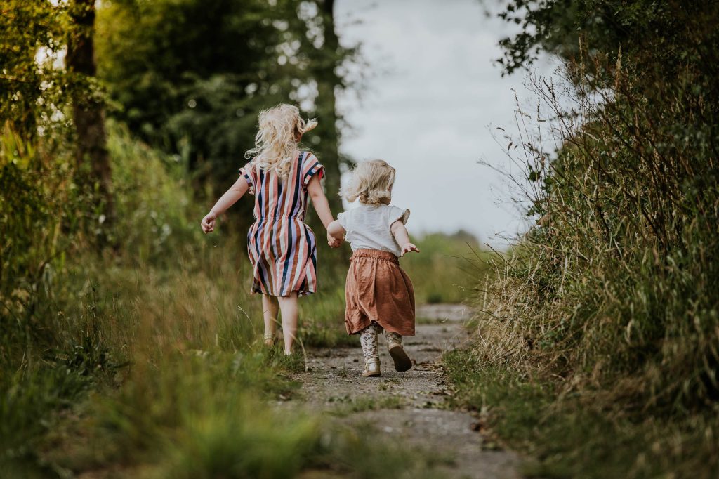 Fotograaf Friesland. Kinderportret door Nickie Fotografie. Zusjes lopen op verlaten landweggetje.