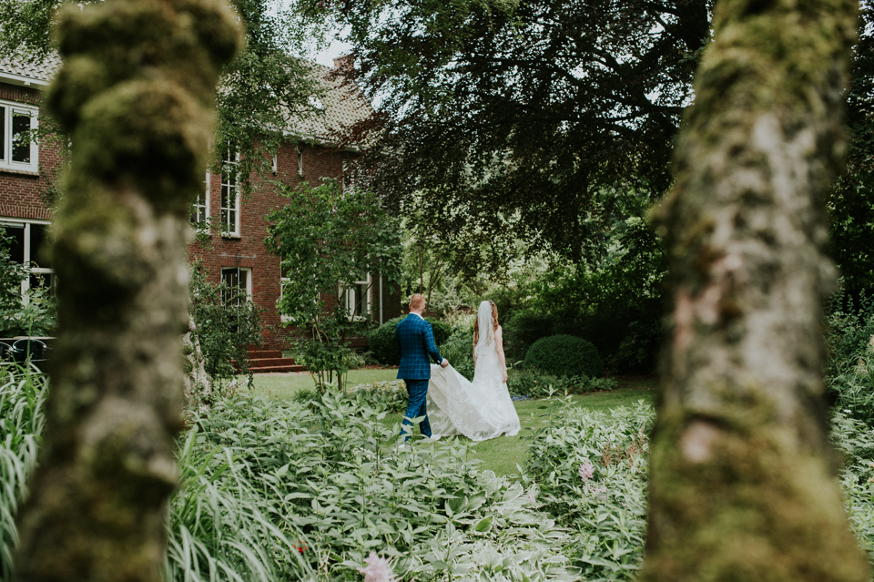 Bruidegom helpt met sleep van bruidsjurk in kloostertuin van Karmelklooster Drachten, Friesland. Bruidsreportage door trouwfotograaf Nickie Fotografie.