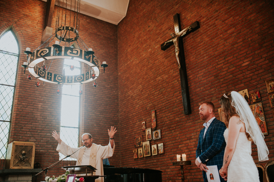 Bruidspaar krijgt de zegen van de voorganger in Karmelklooster Drachten. Trouwreportage door trouwfotograaf Nickie Fotografie.