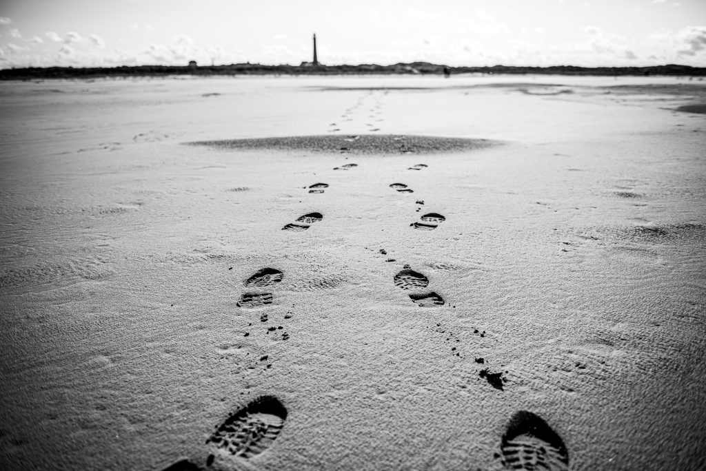 Zwart/wit foto van voetstappen op het strand naar de vuurtoren toe van Schiermonnikoog. Fotoreportage door fotograaf Nickie Fotografie