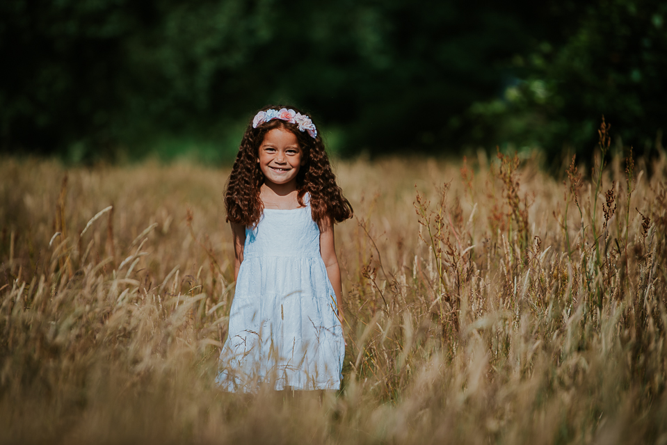 Portret van meisje in wit jurkje met bloemen haarband in het hoge gras door fotograaf Nickie Fotografie uit Dokkum, Friesland