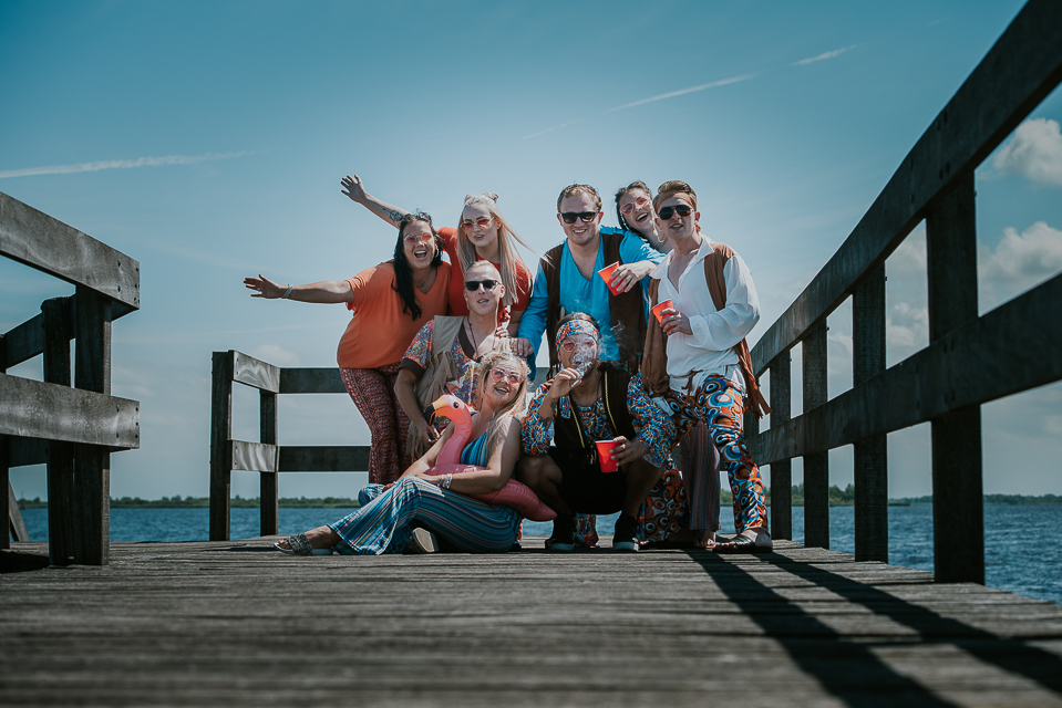 Enthousiaste groepsfoto in hippie kleding op een steiger bij het Lauwersmeer door portretfotografe Nickie Fotografie uit Dokkum
