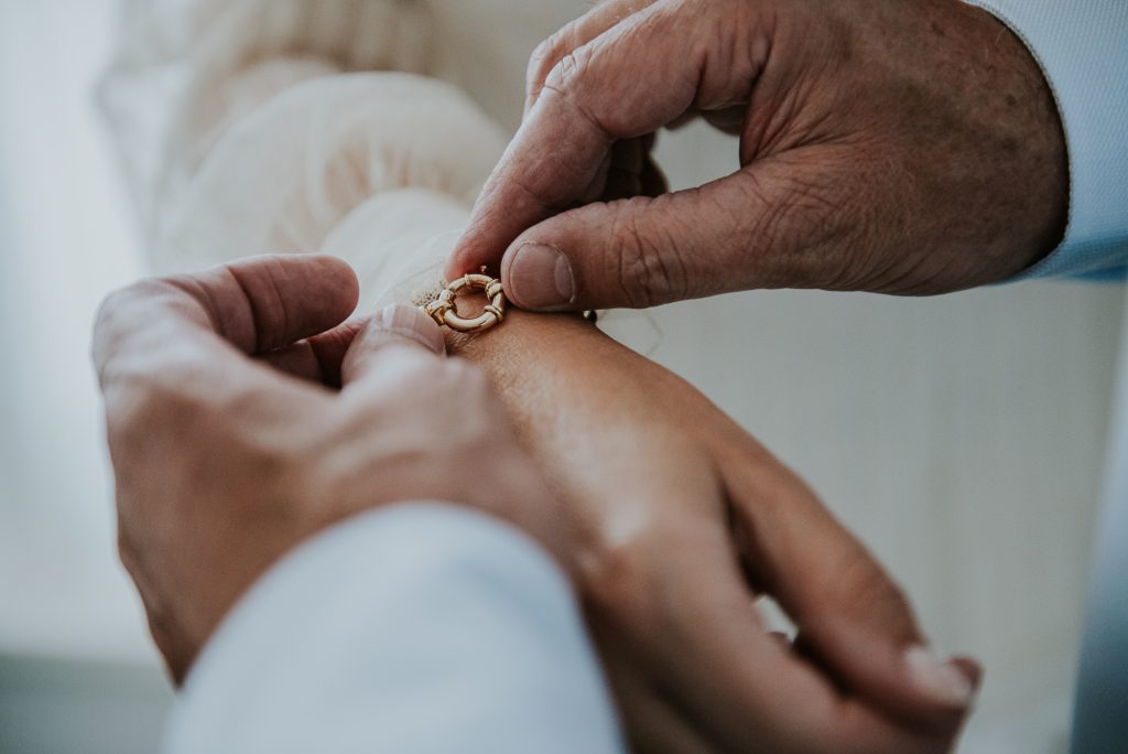 Bruidegom helpt met het omdoen van de armband. Bruidsreportage door fotograaf Nickie Fotografie uit Dokkum, 
Friesland