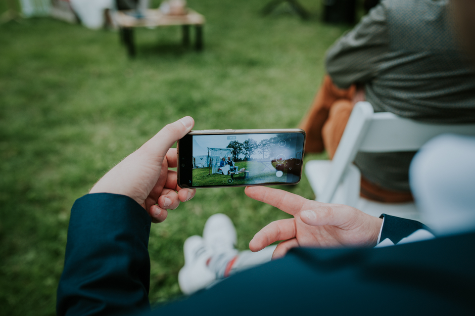 De trouwceremonie wordt gefilmd door een daggast op zijn telefoon. Bruidsfotografie door bruidsfotograaf Nickie Fotografie