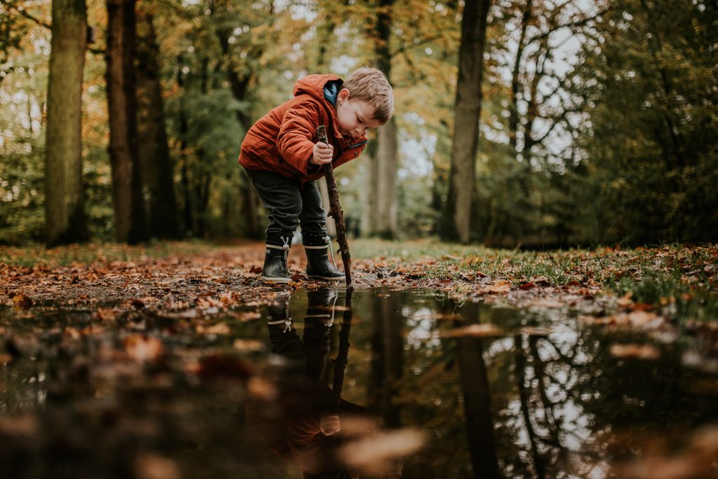 peuter aan het spelen in de herfst met stok en waterplas. Fotosessie door fotograaf NIckie Fotografie uit Dokkum, Friesland