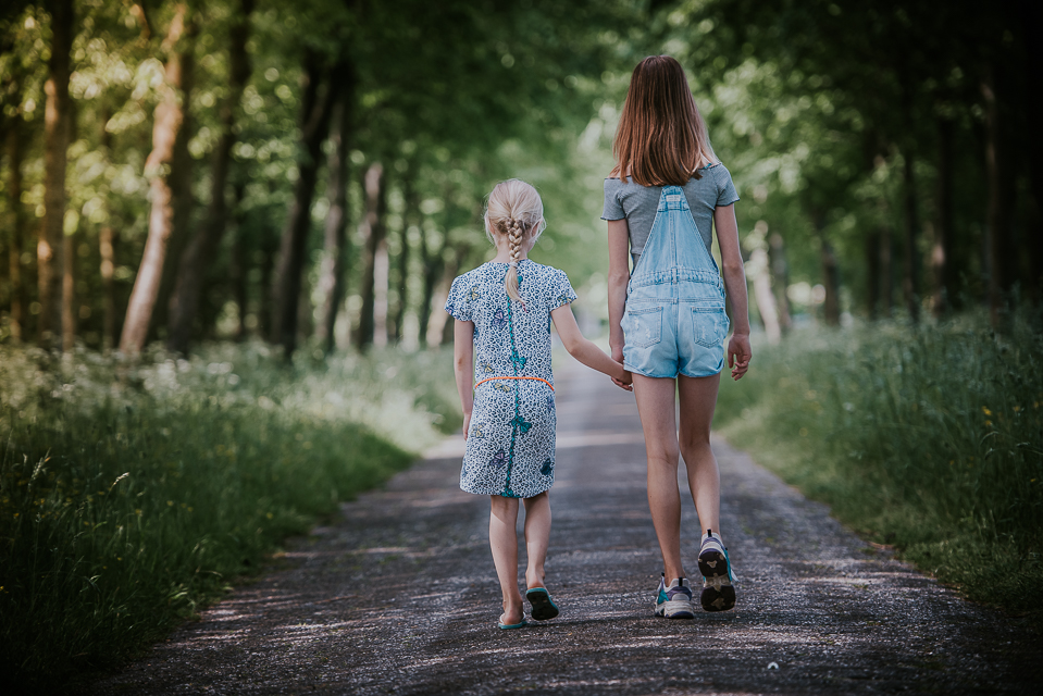Zusjes hand in hand wandelend over een landweggetje, door Nickie fotografie