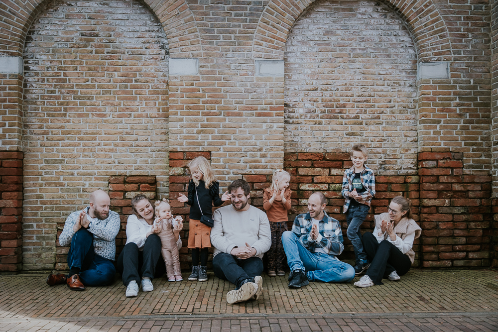 Familieshoot bij de poort van Esonstad door fotograaf Nickie Fotografie uit Friesland. De familie zit op de grond voor de muur.