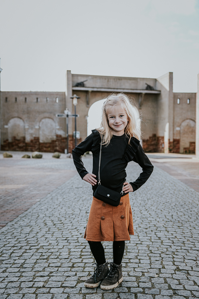 Portret van meisje met de handen op de heupen voor de poort van Esonstad. Fotoshoot door fotograaf Nickie Fotografie uit Friesland.