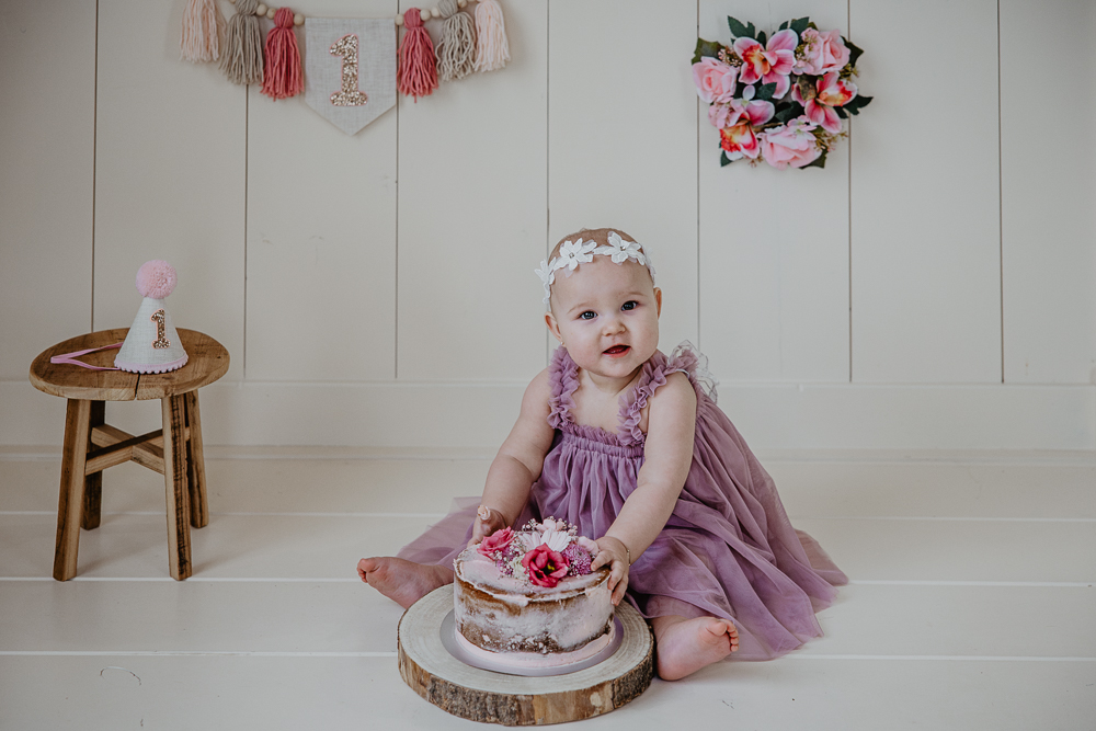Fotograaf Friesland. Cakesmash in roze en paarse tinten. Meisje viert haar 1e verjaardag met naked cake met echte bloemen. Fotoshoot door Nickie Fotografie uit Dokkum.