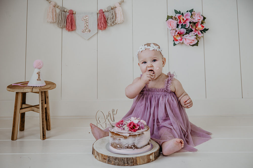 Fotograaf cakesmash Friesland. Jarig meisje eet haar roze taart met echte bloemen. Portret door Nickie Fotografie uit Dokkum.