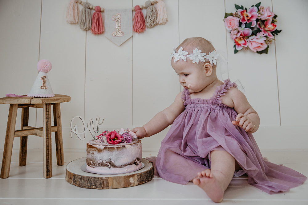 Fotograaf cakesmash Friesland. Jarig meisje eet haar roze taart met echte bloemen. Portret door Nickie Fotografie uit Dokkum.