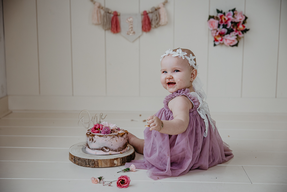 Cakesmash Friesland. Meisje in paars jurkje met vleugels/feeenjurkje bij een naked cake met echte bloemen. Kinderfotografie door Nickie Fotografie uit Dokkum.