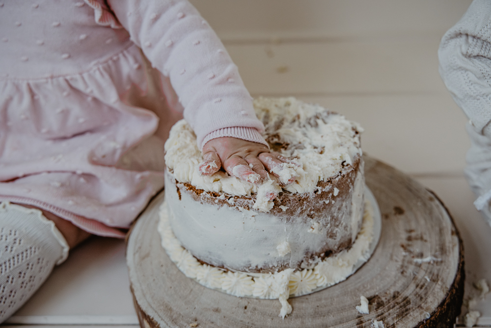 Meisje zit met haar handje in de taart. Babyfotografie door fotograaf Nickie Fotografie uit Dokkum, Friesland.
