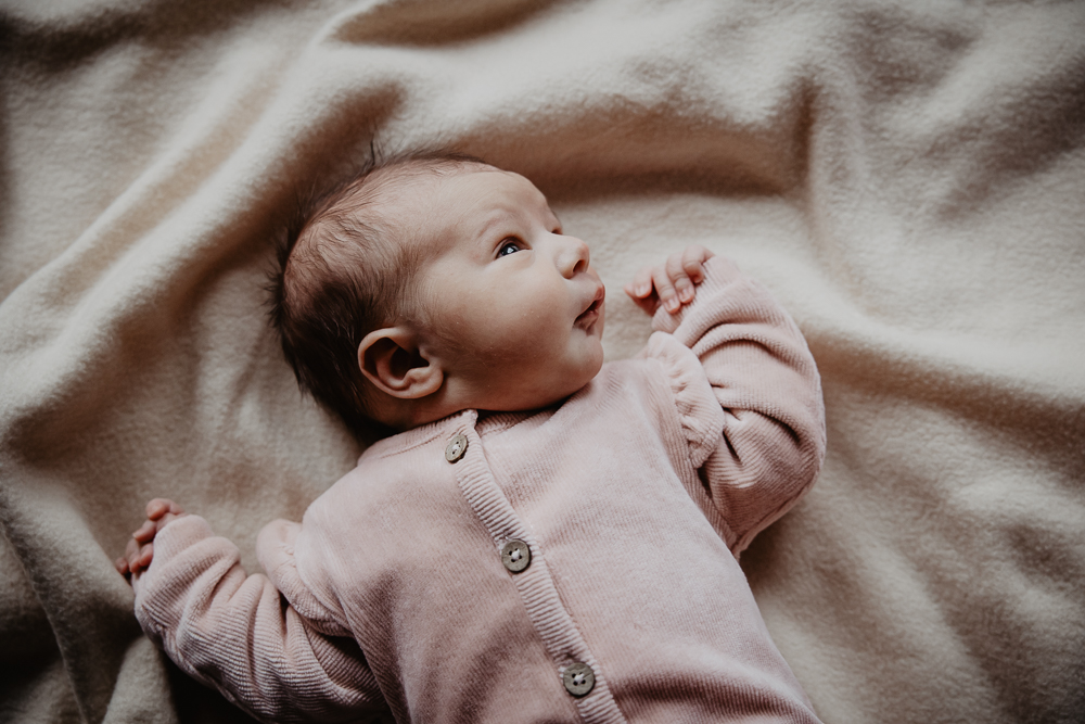 Newborn fotoshoot Heerenveen, Friesland, door fotograaf Nickie Fotografie. Baby meisje in roze pakje ligt op het dekentje en kijkt nieuwschierig om haar heen.
