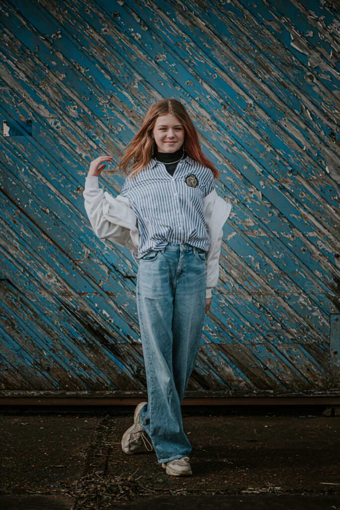 Modeshoot Dokkum door fotograaf NIckie Fotografie. Portret van meisje voor een diagonale blauwe verweerde houten schuurdeur.