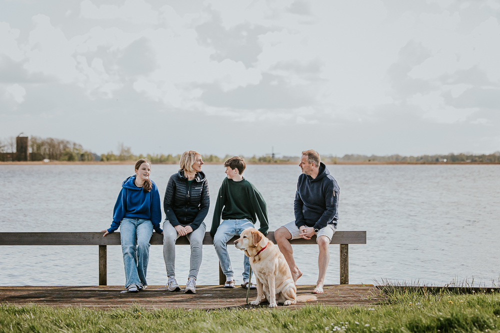 Gezinsportret bij het water. Het gezin met hond zit op een hekje bij Eetjemeer. Gezinsreportage door fotograaf Nickie Fotografie uit Friesland.