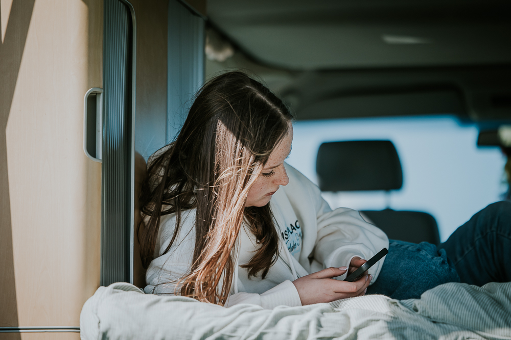 Camperlife. Tiener zit in de camper met haar telefoon. Lifestyle campingshoot door fotograaf Nickie Fotografie uit Friesland.