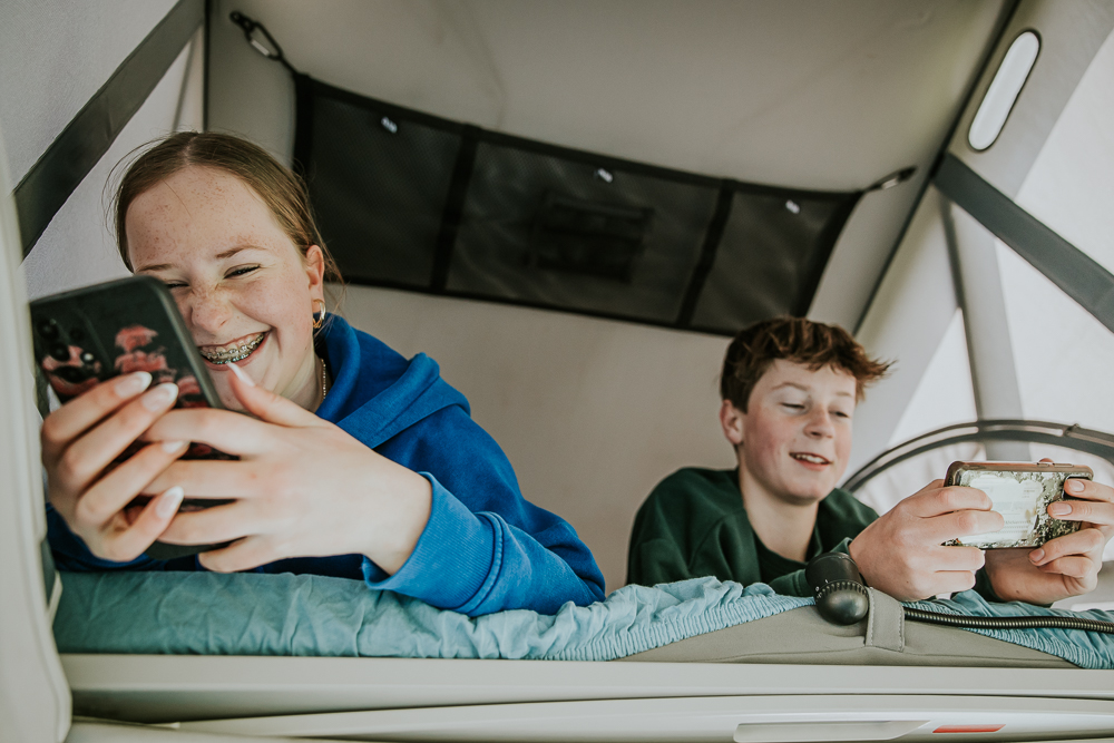 De kinderen spelen op hun telefoon in de camper. Lifestyle campingsfotografie door fotograaf Nickie Fotografie uit Friesland.