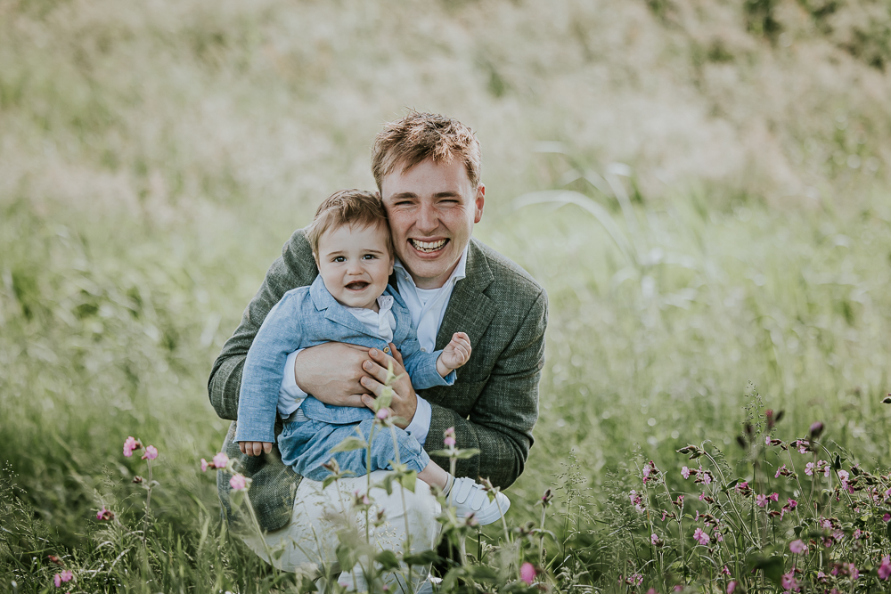 Trouwfotografie Friesland. Portret van bruidegom met zijn zoontje zittend in het hoge gras. Trouwreportage door Nickie Fotografie.