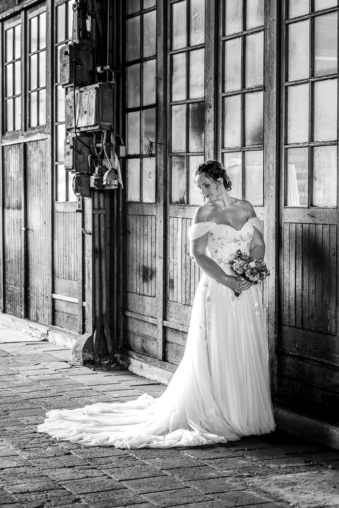 Bruidsshoot in de Sluisfabriek.  Zwart-wit portret van de bruid, bij de oude houten muur in de grote hal, door fotograaf NIckie Fotografie uit Friesland.