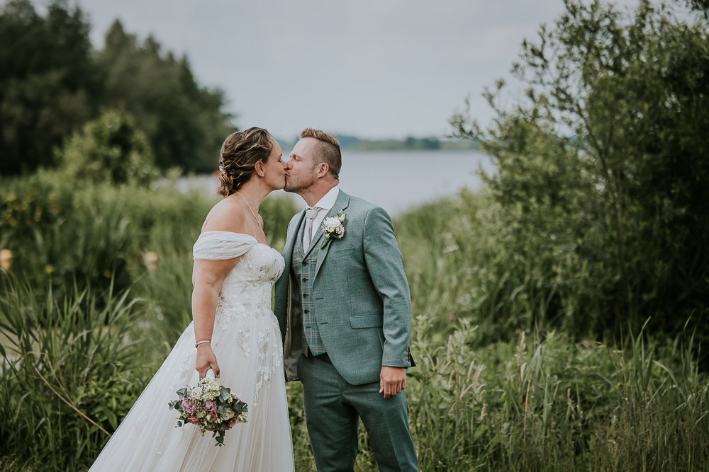 Trouwen bij de Leyen. Kussende bruidspaar tijdens de fotoshoot met water en riet op de achtergrond. Huwelijksfotografie door bruidsfotograaf Nickie Fotografie uit Friesland.