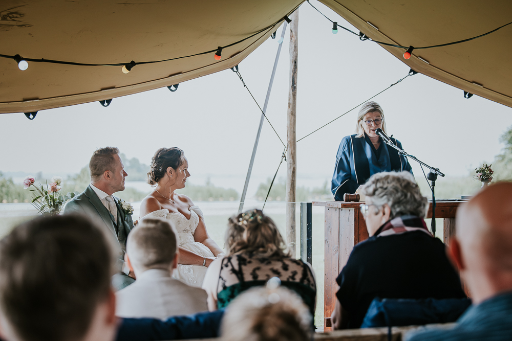 Trouwen bij de paviljoen de Leyen. Het bruidspaar luistert aandachtig naar de trouwambtenaar. Trouwreportage door bruidsfotograaf Nickie Fotografie uit Friesland.