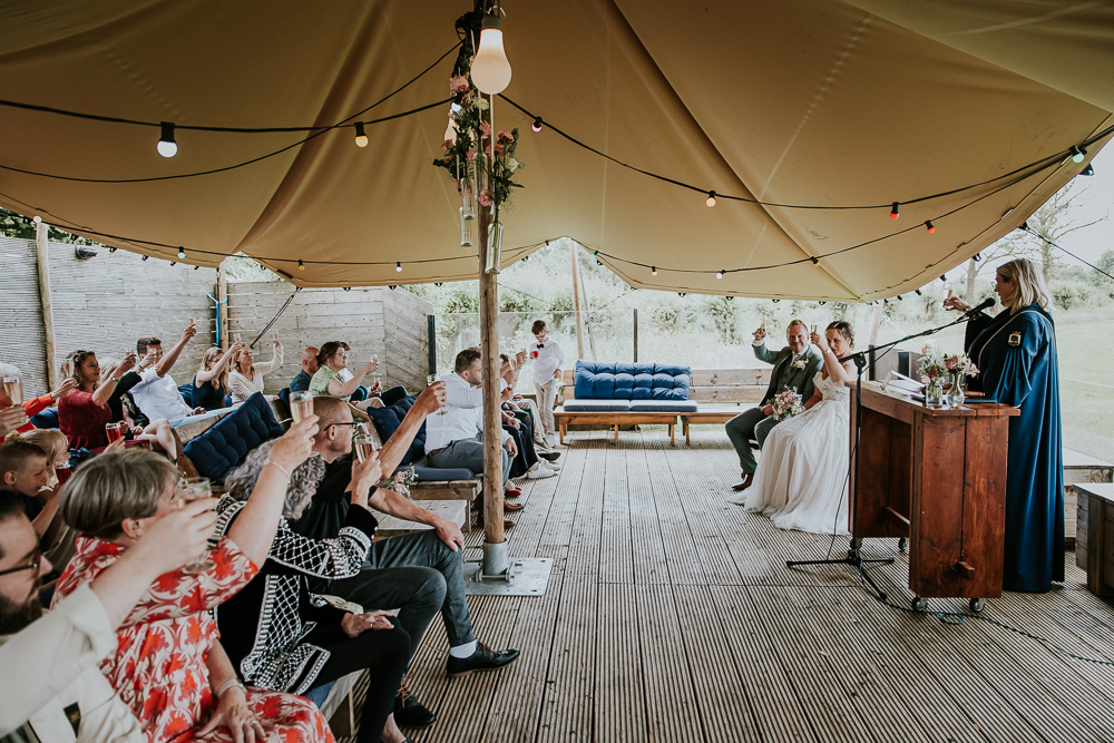 Proosten op het bruidspaar in de trouwtent op het terras van strandpaviljoen de Leyen. Trouwreportage door huwelijksfotograaf Nickie Fotografie uit Friesland.