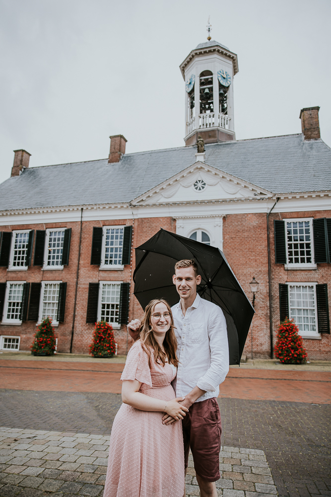 Trouwen in Dokkum. Het aanstaande bruidspaar poseert onder de paraplu voor het oude Stadhuis van Dokkum.    Trouwreportage door bruidsfotograaf Nickie Fotografie.